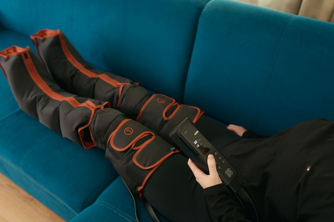 Drenaż limfatyczny nóg. Co daje i jak go wykonać w domu? Na zdjęciu kobieta leżąca na sofie i aparat do drenażu limfatycznego ZENT® AirPress™ – presoterapia i masaż limfatyczny nóg, który ma założony na nogi